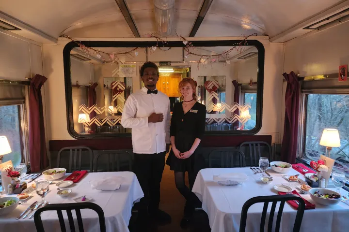 Two servers stand in a vintage dining car, preparing a romantic Valentine’s dinner service aboard the Tennessee Valley Railroad.