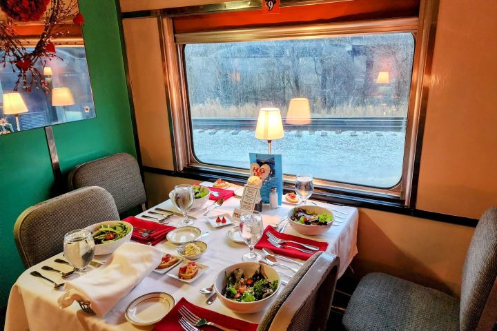 Elegant dining table set for two aboard the Tennessee Valley Railroad Valentine Train Ride, featuring fine china, red napkins, and candlelight by the window.