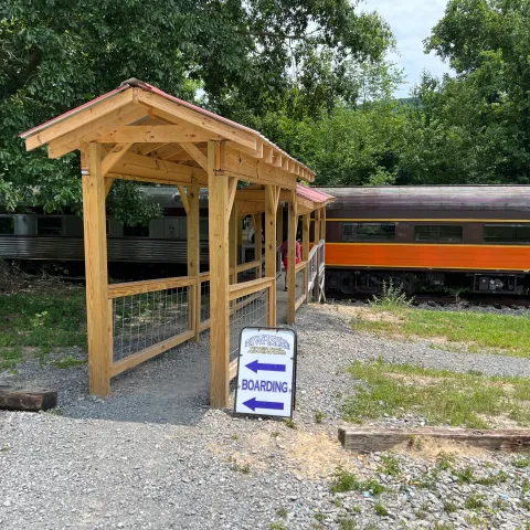 A TVRM passenger train crossing the Hiwassee River area on the Hiwassee Loop, surrounded by trees and mountain scenery.