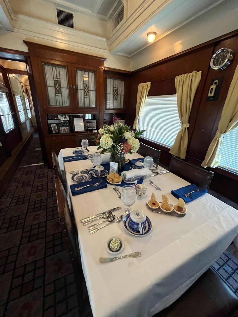 Elegant dining setup with white tablecloth, blue dishes, and floral centerpiece in a wood-paneled room.
