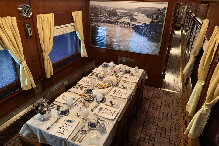 Vintage private railcar dining room with formal table settings and scenic artwork on the wall.
