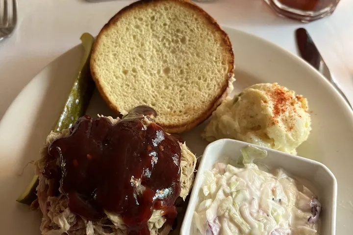 Sandwich with BBQ sauce, coleslaw, and potato salad on a plate.