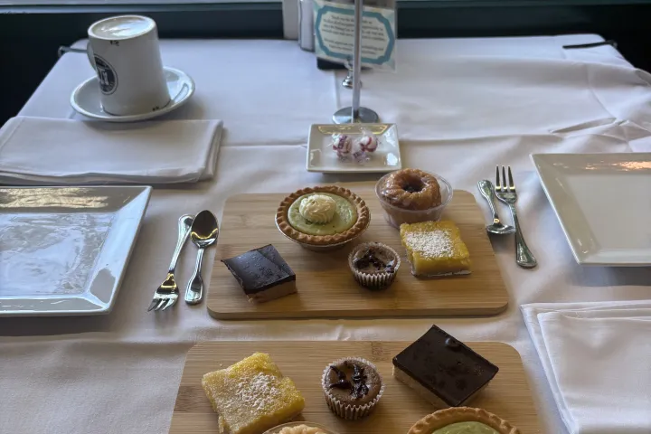 Assorted desserts on wooden boards on a dining table by a window.