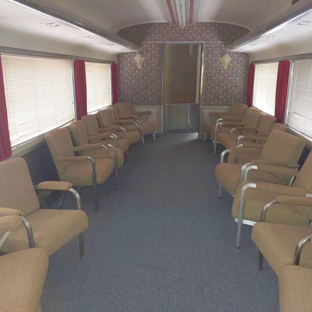 Vintage train car interior with rows of brown seats and floral wall design.