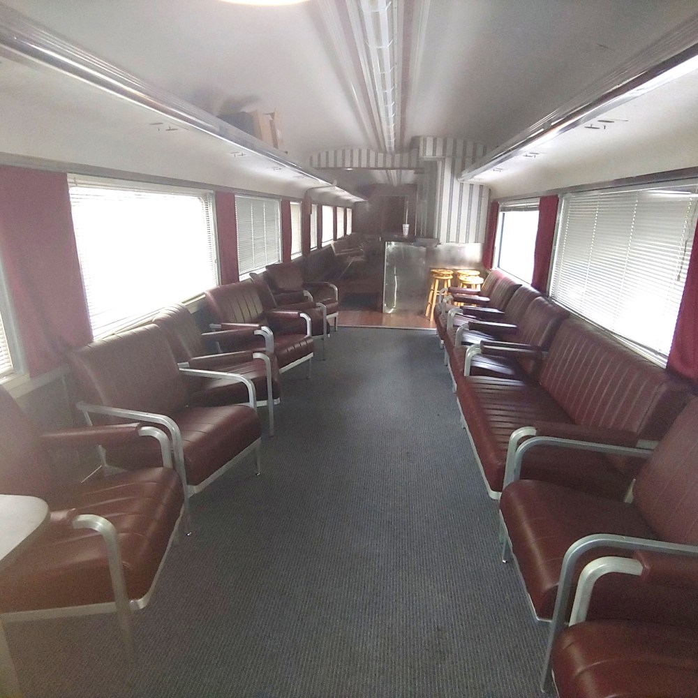 Interior of a vintage train car with red cushioned seats and a small bar at the end.