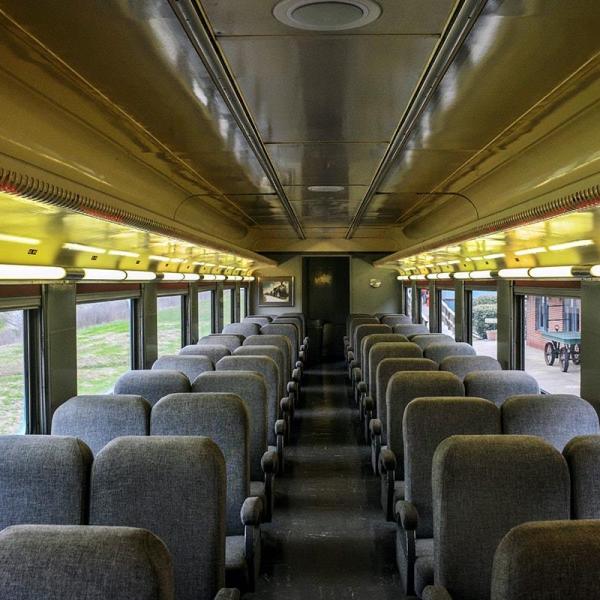 Interior view of a Tennessee Valley Railroad Museum passenger coach with rows of comfortable gray seats, large windows, and a warm yellow ceiling lighting.