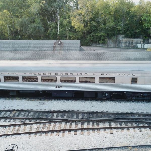 Aerial view of the Richmond, Fredericksburg & Potomac passenger railcar labeled 857 parked on a railway track near a building and surrounded by greenery.