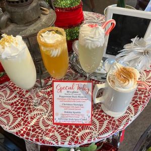 Four festive drinks on a lace table with a small menu and holiday decor.