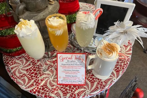 Four festive drinks on a lace table with a small menu and holiday decor.