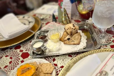 Tea table with scones, cream, and holiday decor on a lace tablecloth.