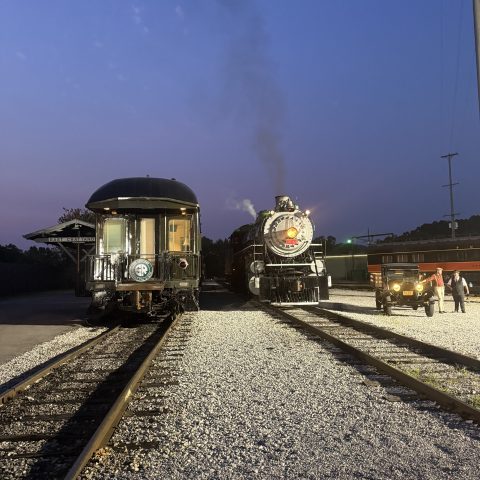 Two vintage trains on parallel tracks at dusk with bright headlights.