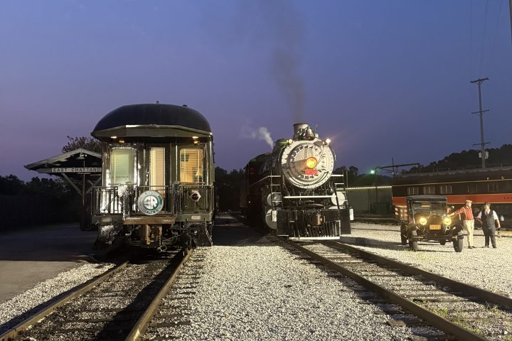 Two vintage trains on parallel tracks at dusk with bright headlights.