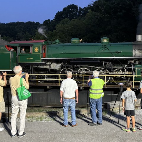 People observe a vintage green steam locomotive on display.