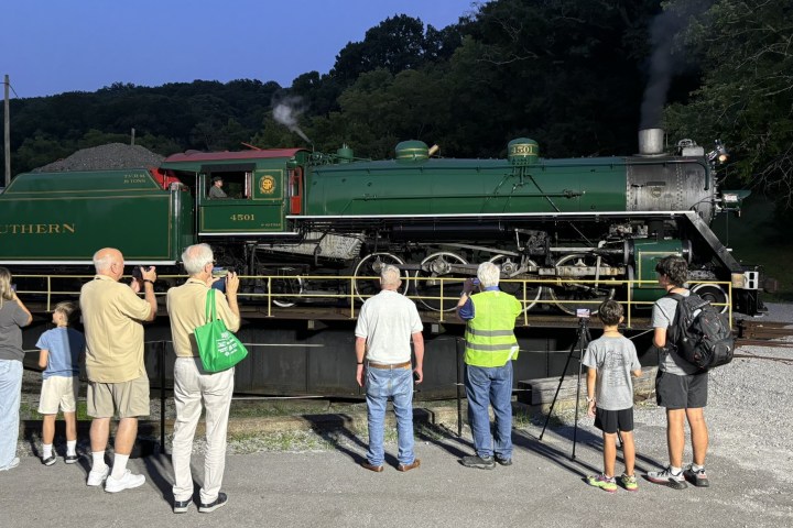 People observe a vintage green steam locomotive on display.