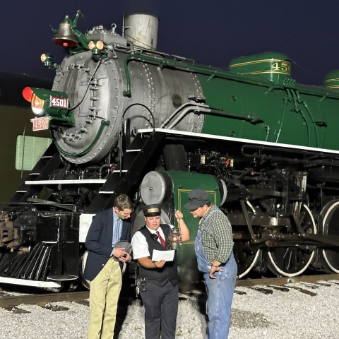 Three people standing by a green steam locomotive at night.