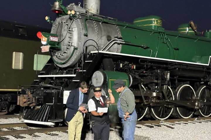 Three people standing by a green steam locomotive at night.