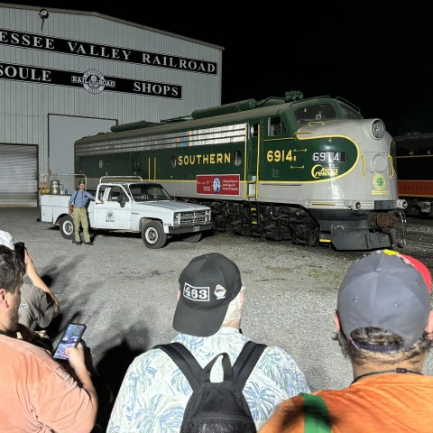 People gather around a vintage Southern 6914 train engine at a railway shop.