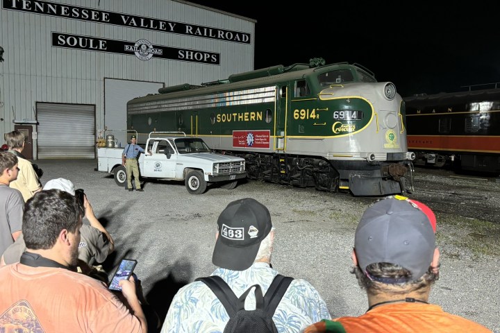 People gather around a vintage Southern 6914 train engine at a railway shop.