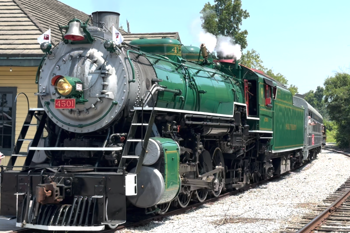 Green steam locomotive stopped at a train station platform.