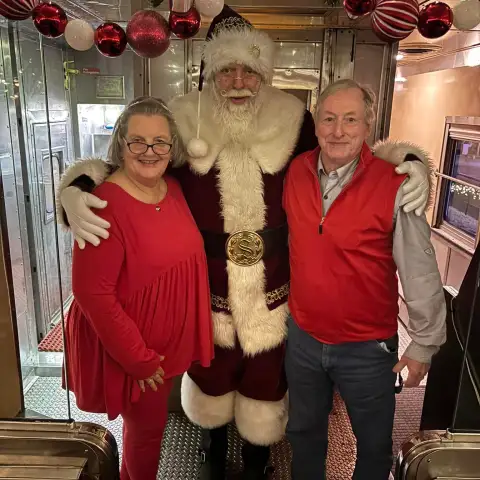 Santa with two people in a festive train decorated with red and white ornaments.