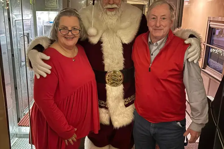 Santa with two people in a festive train decorated with red and white ornaments.
