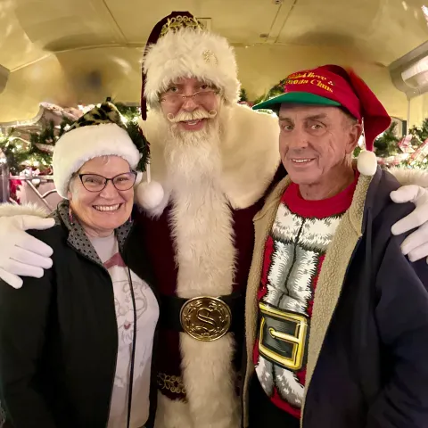 Santa smiling with two guests during the Nightcap With St. Nick 21+ Christmas train ride at the Tennessee Valley Railroad Museum.