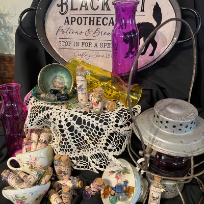 Vintage apothecary display with potion bottles, lace, and lantern on black cloth.