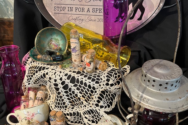 Vintage apothecary display with potion bottles, lace, and lantern on black cloth.