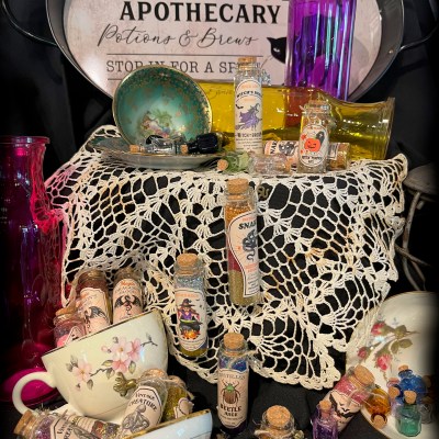 Apothecary setup with potions, bottles, lace cloth, teacups, and a Black Cat sign.