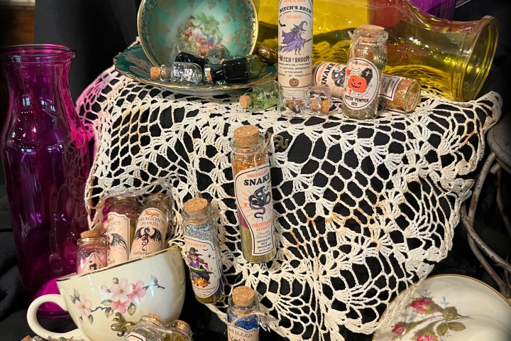 Vintage apothecary setup with potion bottles, teacups, and crochet tablecloth on black fabric.