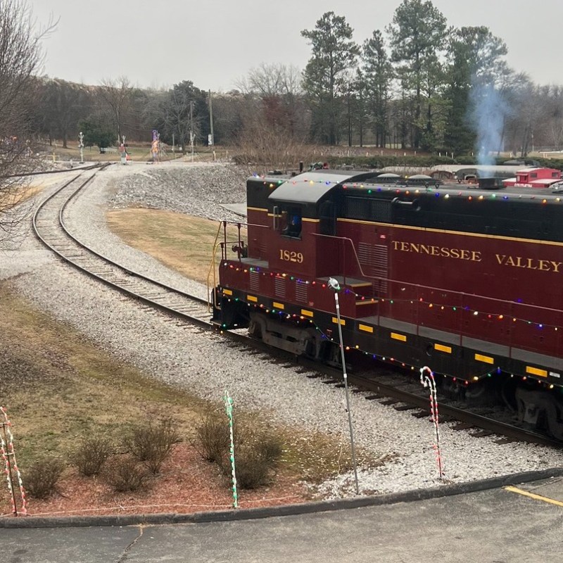 A Tennessee Valley Railroad Museum locomotive decorated with holiday lights and festive displays at night.