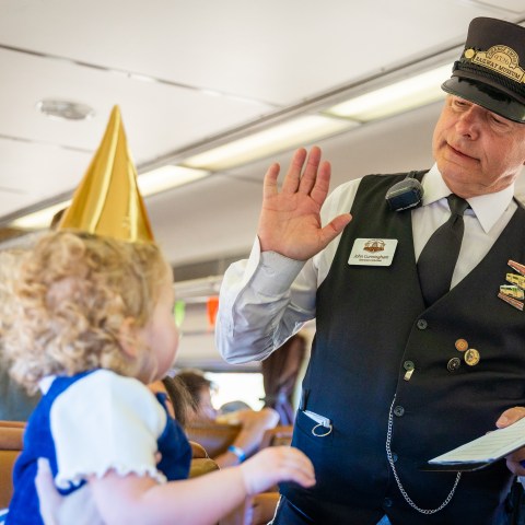 A child wearing a gold party hat high-fiving a conductor on a train during the Day Out with Thomas event.