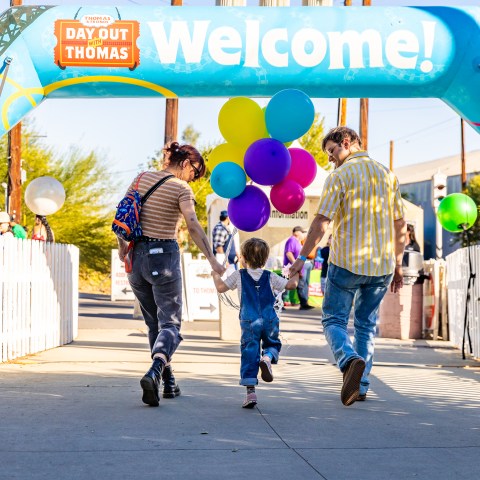 Family walking under the Day Out with Thomas welcome arch, holding hands and balloons.