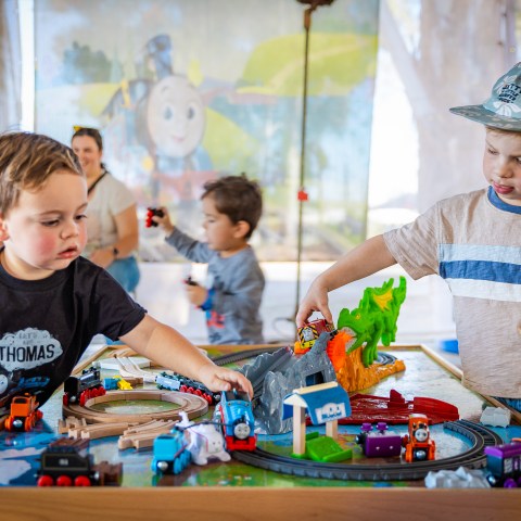 Kids playing with a Thomas toy train set, including colorful tracks, bridges, and toy trains, during a Day Out with Thomas event.