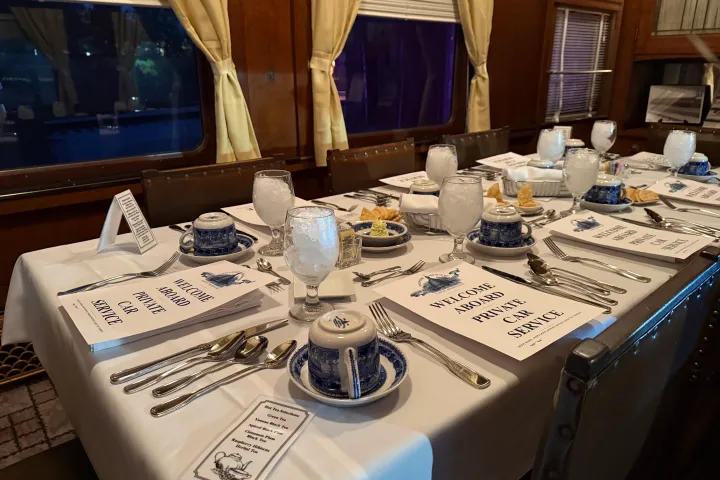 Elegant holiday table setting inside a vintage train dining car, featuring menus, china, and festive décor.
