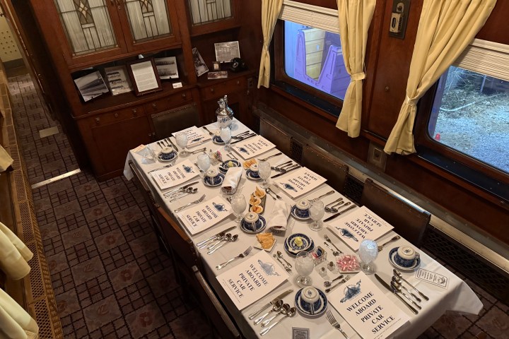 Formal dining setup in a vintage train car with elegant holiday décor, set tables, and warm ambient lighting.