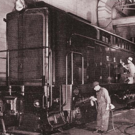 Two workers painting a large train locomotive inside an industrial building.