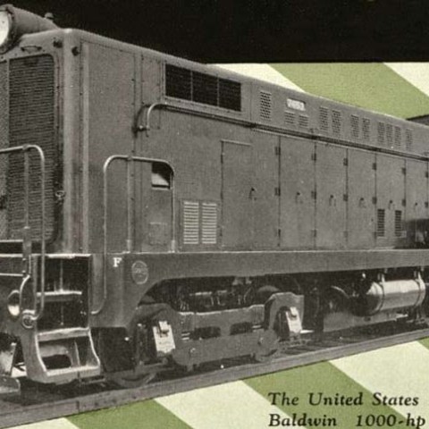 Vintage diesel-electric locomotive used by U.S. Army, shown on a green and white striped background.