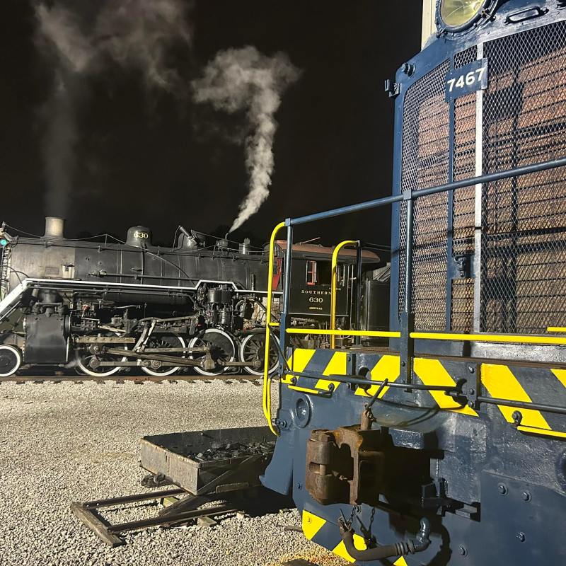 Steam train and locomotive at night on a gravel track, steam rising.