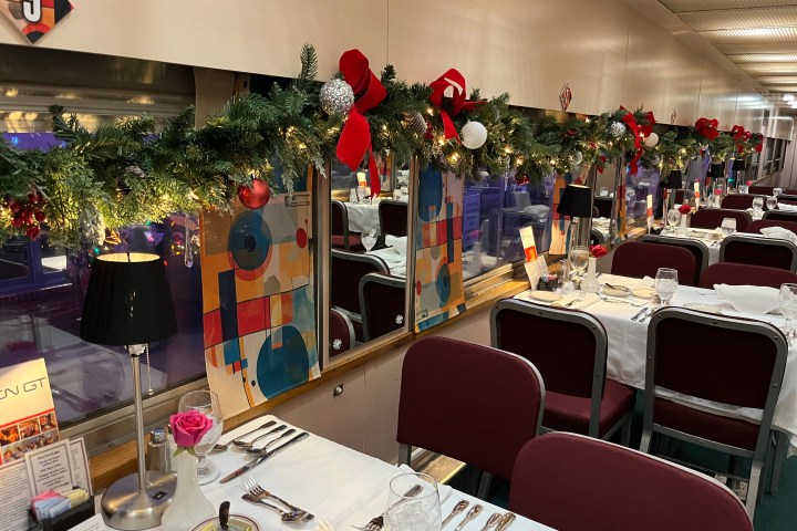 Dining car with festive garland, tables set with white cloths and dark red chairs.