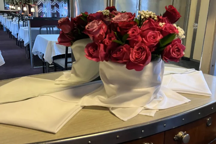 Red roses in a white cloth vase on counter in a decorated dining car.