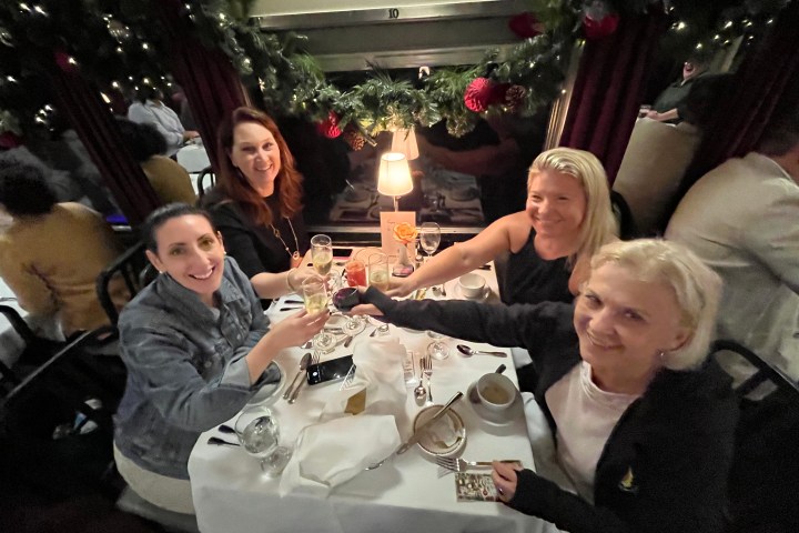 Four women toasting with drinks at a festive, decorated dining table.