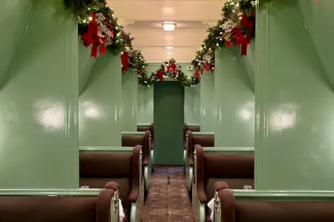 Train car interior with green walls, brown seats, and festive garlands with red bows.