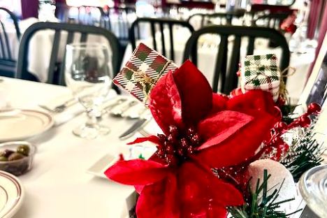 Festive dining table with red poinsettia centerpiece in a decorated train car.