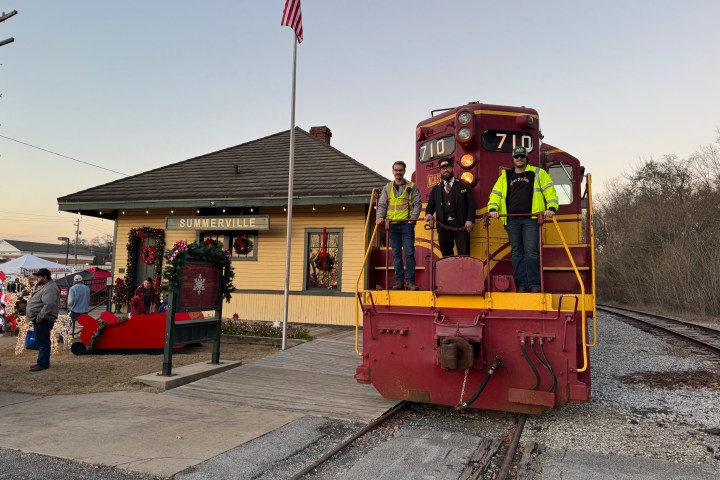 Train with three people next to festive station and holiday decorations in Summerville.