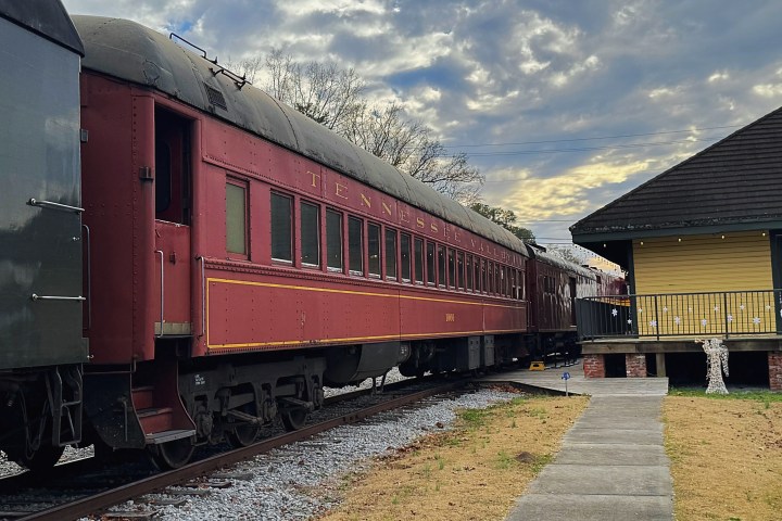 Red train car on tracks beside a yellow building under a cloudy sky.