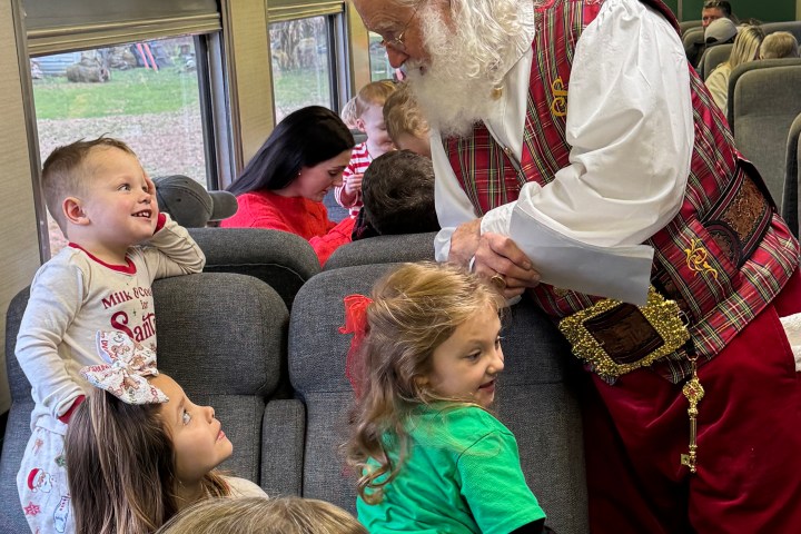 Santa talking to delighted children on a festively decorated train car.