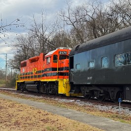 Orange and black holiday-themed train engine parked on the tracks beside the Summerville Depot during the Christmas season.