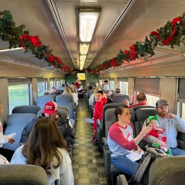 Families in festive attire riding inside a decorated Summerville Christmas train as Santa visits each row.
