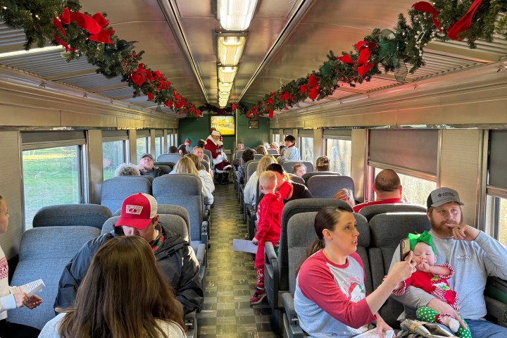 Families in festive attire riding inside a decorated Summerville Christmas train as Santa visits each row.